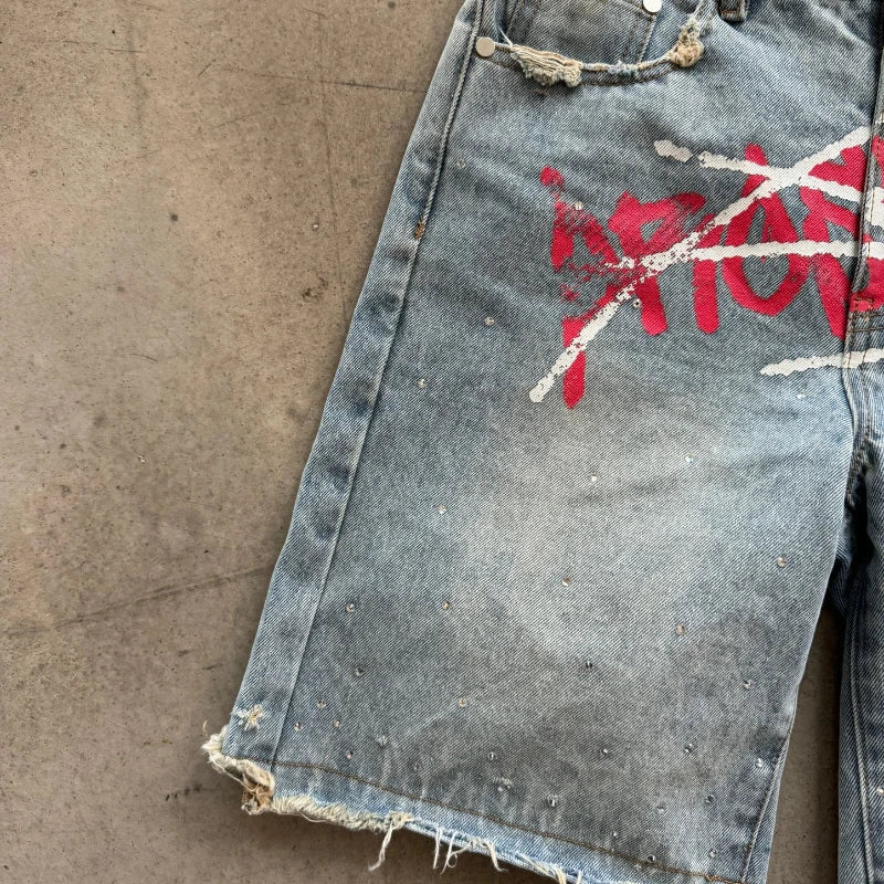 Distressed denim shorts with red and white graphic design on a concrete surface