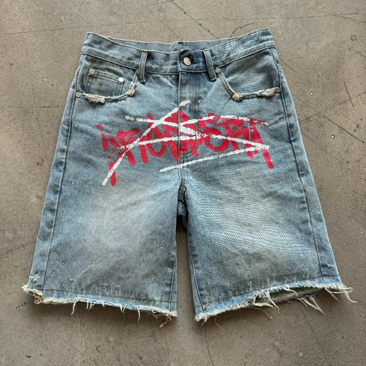 Denim shorts with red and white graphic on a concrete floor