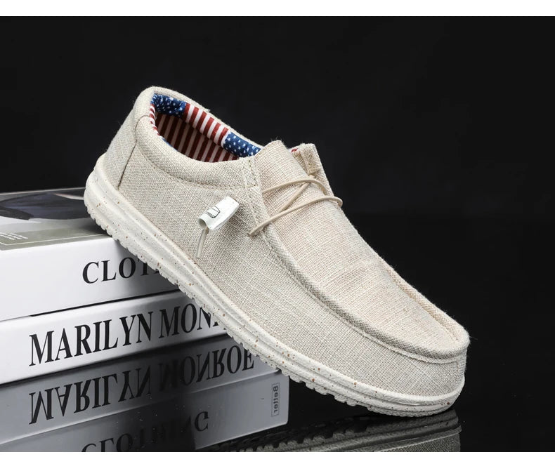 A single beige canvas slip-on loafer-style shoe with a lace detail and white sole, displayed on stacked books against a black background.