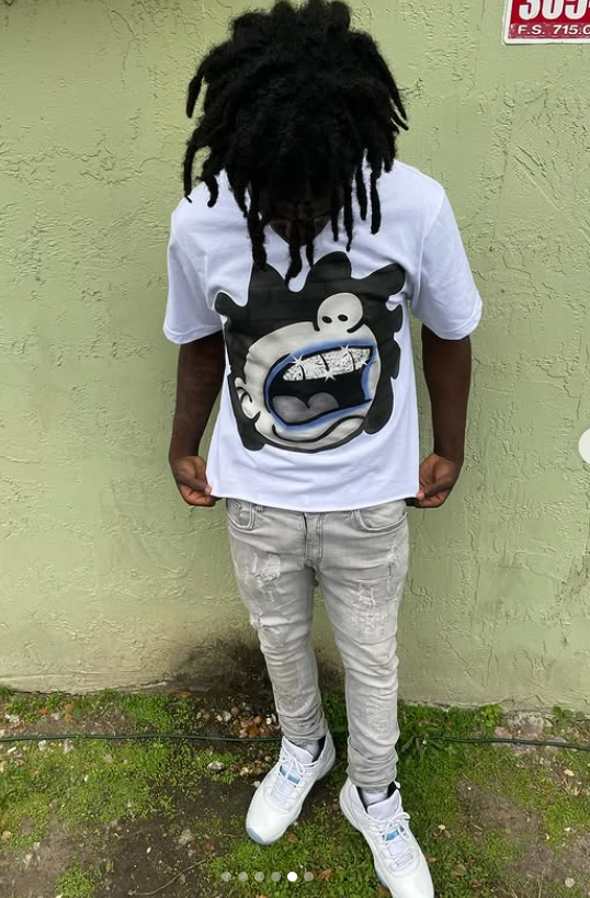 Person wearing a white t-shirt with a graphic design against a green wall.