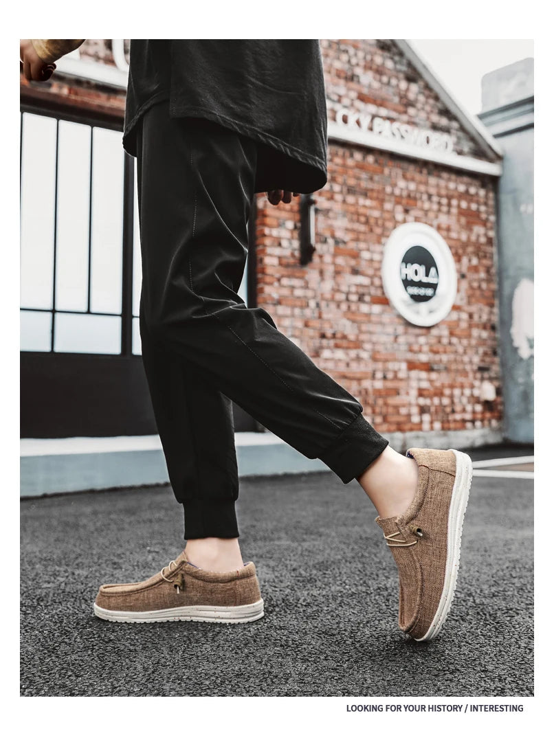 Person wearing brown shoes and black pants in front of a brick wall with a logo.