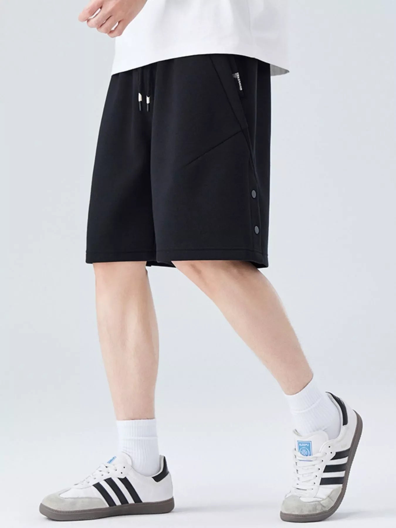 Person wearing black shorts and white sneakers on a light gray background