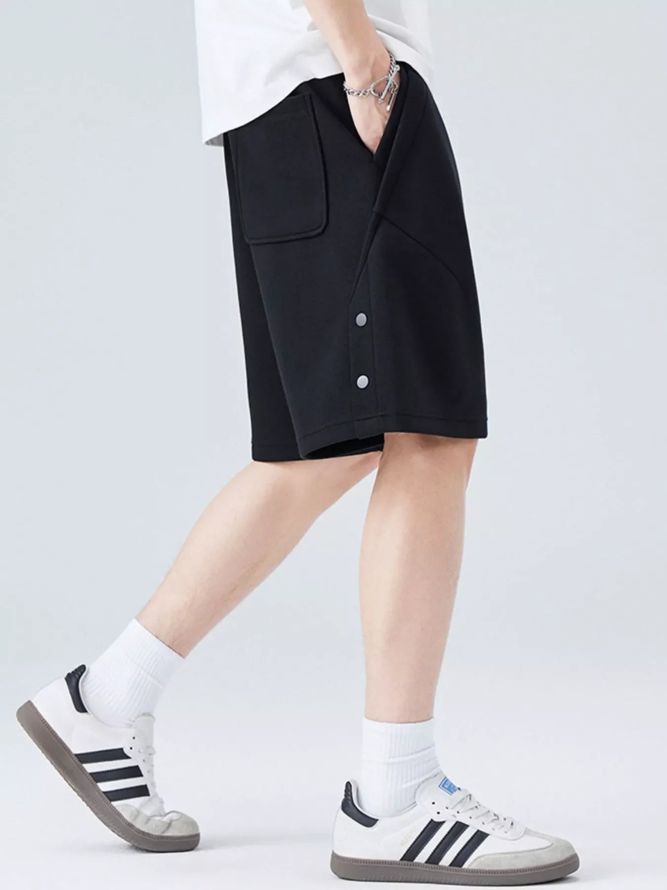 Person wearing black shorts with white sneakers on a plain background